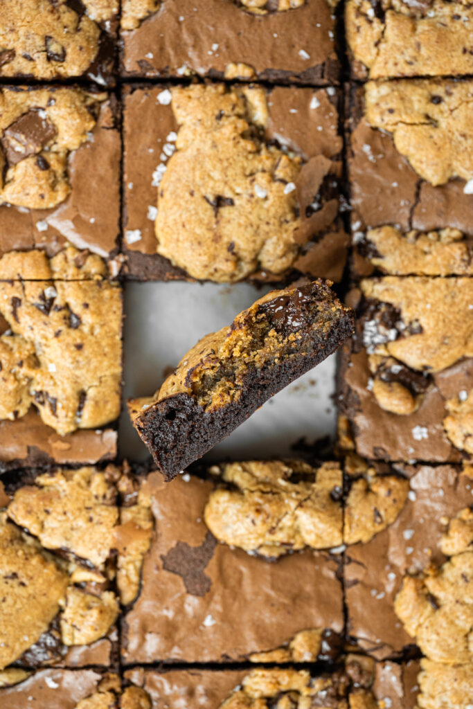 Brookie cortado ao meio, mostrando a textura úmida do brownie com cookie por cima e pedaços de chocolate derretido.