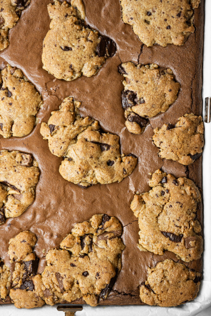 Brookie assado na forma, com massa de cookie espalhada por cima do brownie e pedaços de chocolate visíveis.