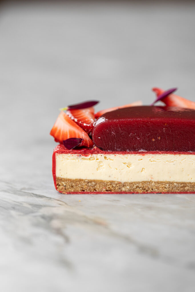 Entremet cheesecake do amor cortado, mostrando camadas de base crocante, cheesecake cremoso e geleia de morango