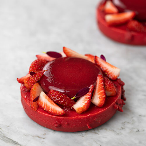 Entremet individual de cheesecake do amor, com cobertura vermelha, morangos frescos e flores comestíveis