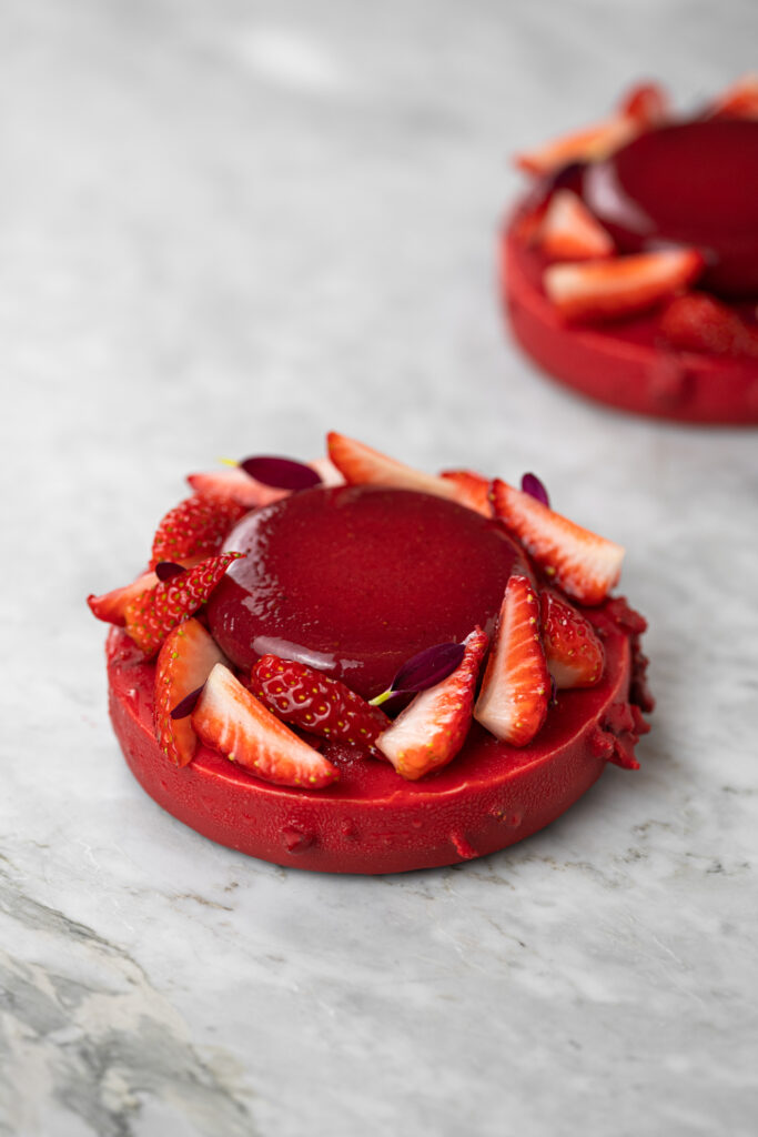 Entremet individual de cheesecake do amor, com cobertura vermelha, morangos frescos e flores comestíveis
