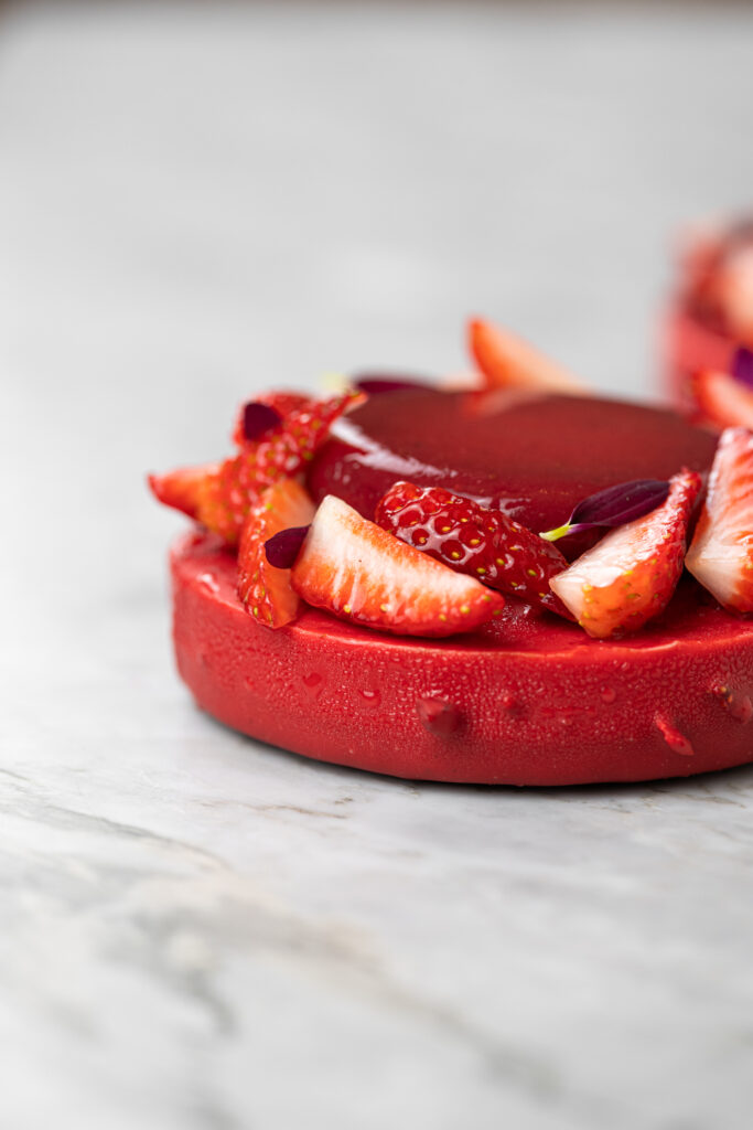 Cheesecake do amor em close lateral, com cobertura vermelha aveludada e decoração de morangos frescos