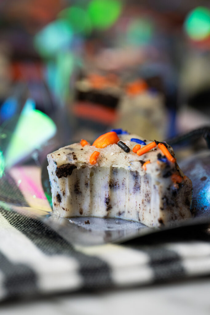 Close-up de um pedaço de fudge de cookies and cream com confeitos coloridos de Halloween, mostrando a textura cremosa e pedacinhos de biscoito.