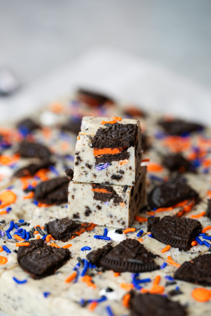 Pedaços de fudge de cookies and cream empilhados, com pedaços de biscoito recheado laranja e confeitos nas cores de Halloween.