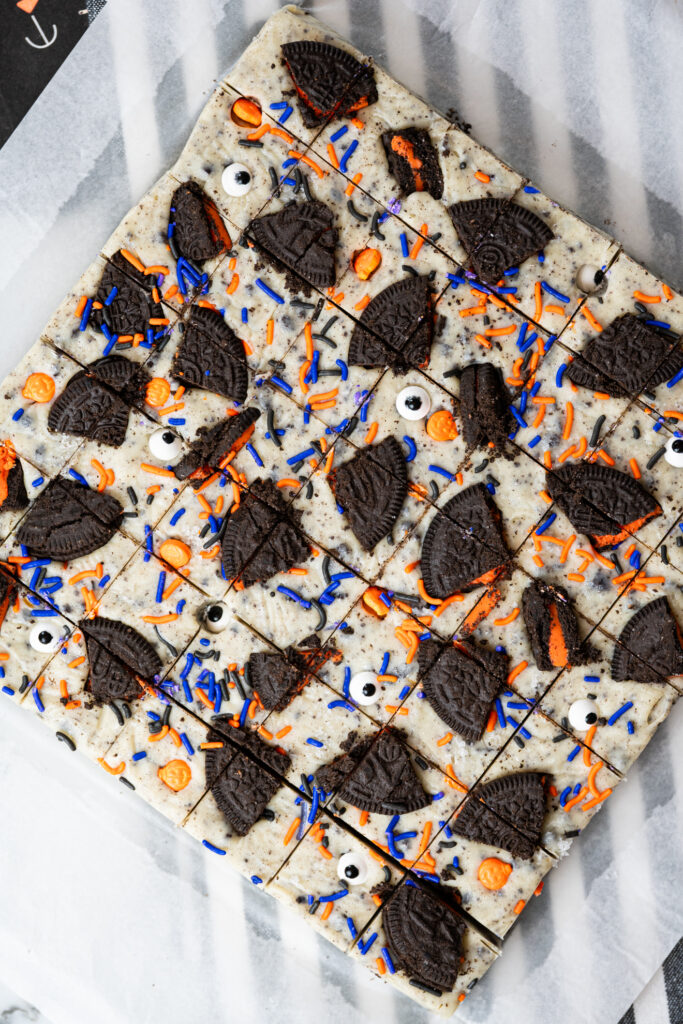 Vista aérea da forma de fudge de cookies and cream decorado com pedaços de biscoito Oreo, confeitos laranja e roxos e olhos de açúcar para o Halloween.