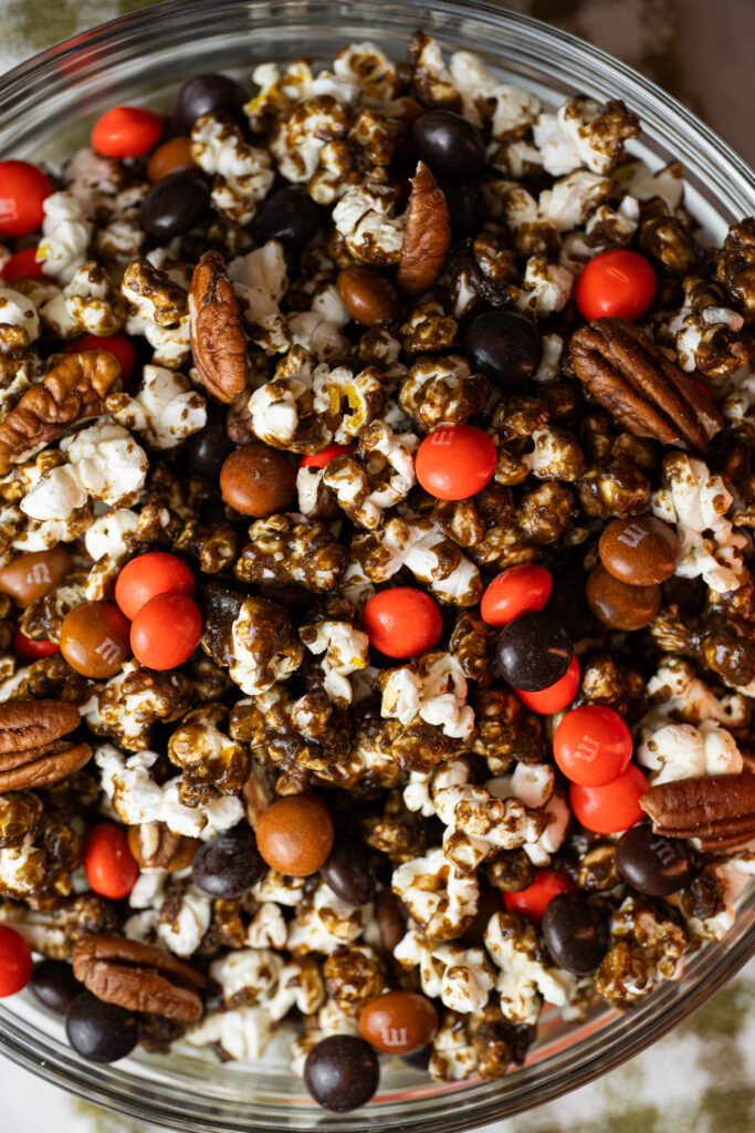Pipoca de Pumpkin Spice com caramelo, M&Ms laranja e marrom e nozes pecan em uma tigela de vidro — receita crocante e colorida para o Halloween.