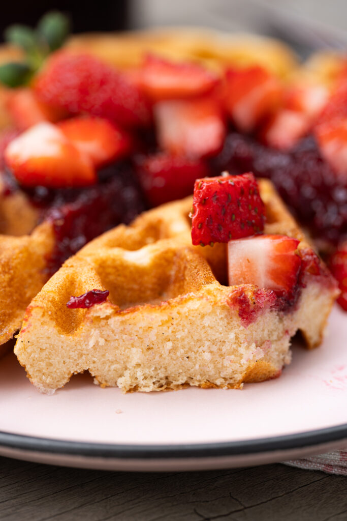 Waffle caseiro crocante e macio cortado ao meio, mostrando a textura interna macia, servido com geleia e morangos frescos.