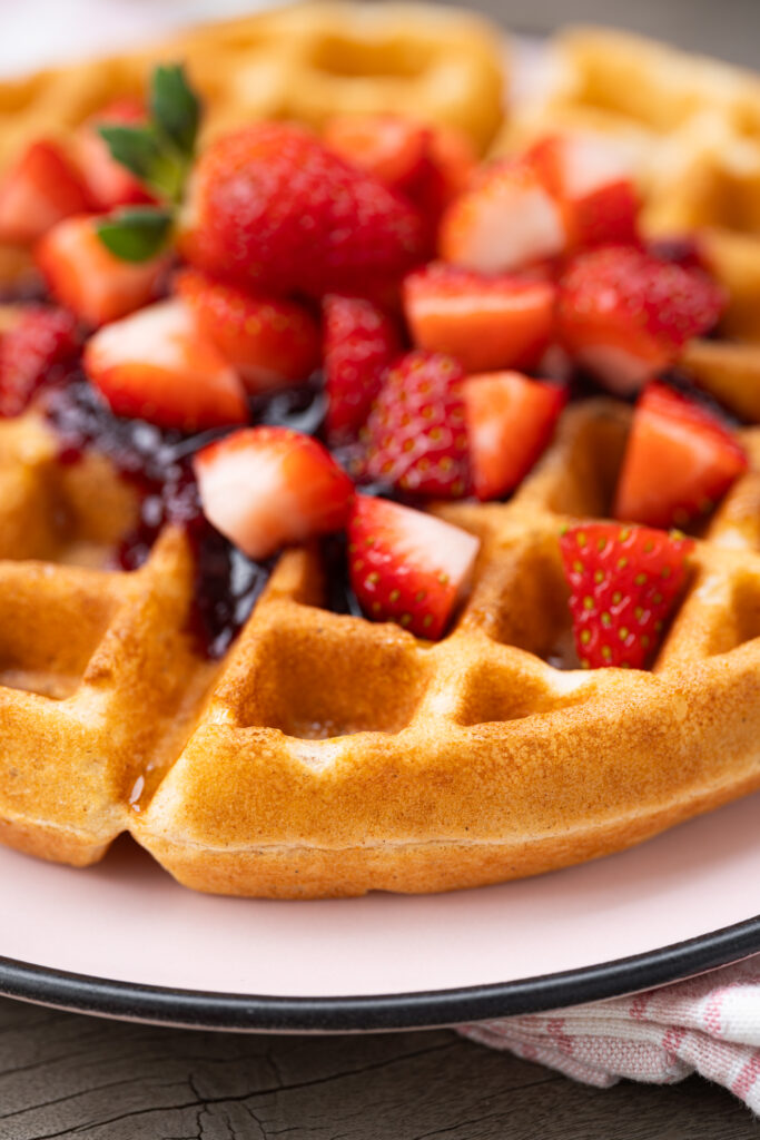 Waffle caseiro crocante e macio cortado ao meio, mostrando a textura interna macia, servido com geleia e morangos frescos.